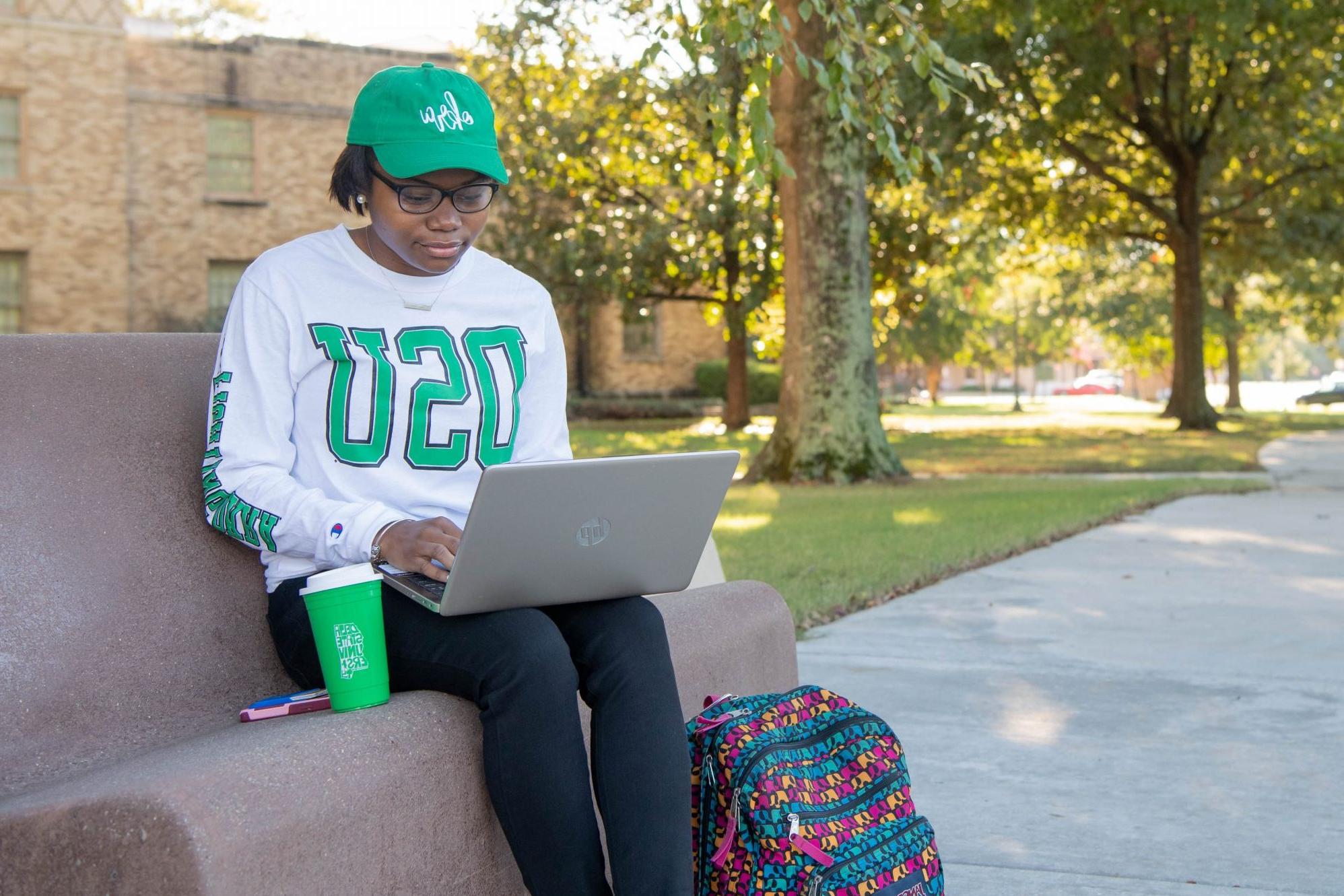 Student sitting outside on campus looking at laptop for scholarship information.